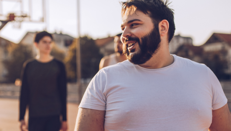 Young overweight man in white tshirt playing basketball with friends