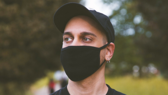 young man wearing black cloth mask stands with arms crossed