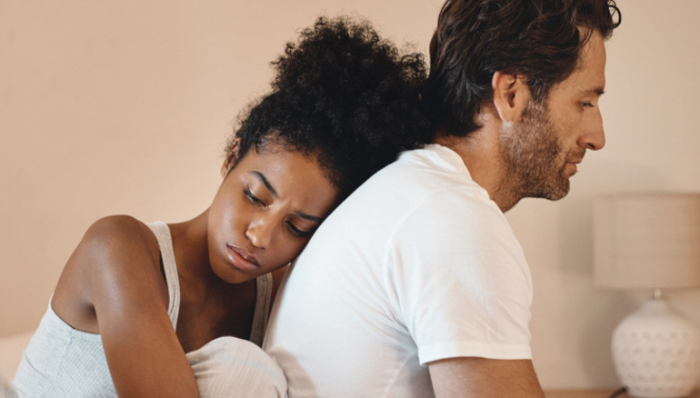 sad couple sits on bed woman holds man from behind